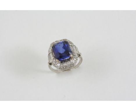 A SYNTHETIC SAPPHIRE AND DIAMOND CLUSTER RING the rounded rectangular-shaped synthetic sapphire is set within a surround of b