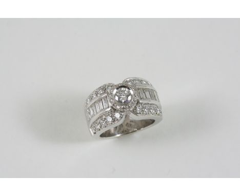 A DIAMOND RING the central brilliant-cut diamond is set within a surround of circular-cut diamonds, with a row of baguette-cu