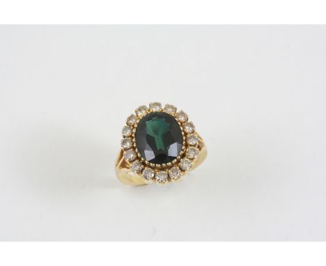 A DIAMOND AND GREEN STONE CLUSTER RING the oval-shaped green synthetic spinel is set within a surround of circular-cut diamon