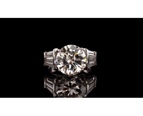 A diamond dress ring, set with a central round brilliant-cut diamond which weighs 5.71cts within tapered baguette-shaped diam