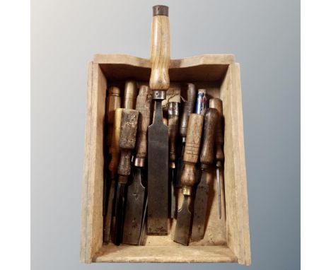 A wooden caddy containing vintage woodworking chisels, various sizes.