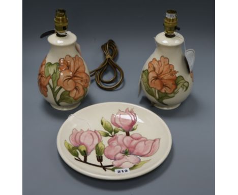 A pair of Moorcroft Hibiscus pattern table lamps and a Magnolia pattern plate, both decorated with pink flowers on a white gr