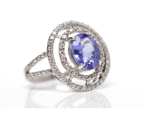 TANZANITE AND DIAMOND RINGthe central oval tanzanite 9.4x7.4mm within an openwork double diamond set border, on diamond set b
