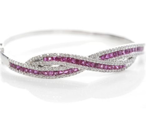 EIGHTEEN CARAT WHITE GOLD RUBY AND DIAMOND BANGLEwith two rows of rubies flanked by rows of diamonds, in a crossover setting,