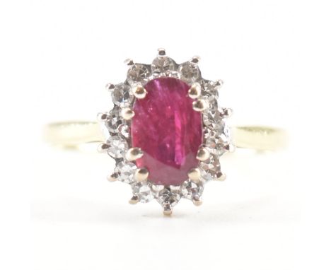 A hallmarked 18ct yellow gold, ruby &amp; diamond cluster ring. The ring having a central oval cut double prong set ruby surr