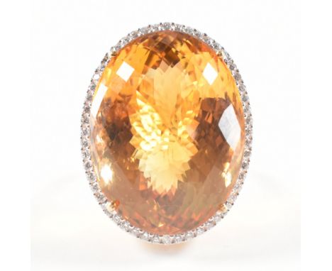 A hallmarked 18ct gold citrine and diamond cocktail ring. The ring being set with a large faceted oval citrine with a halo of
