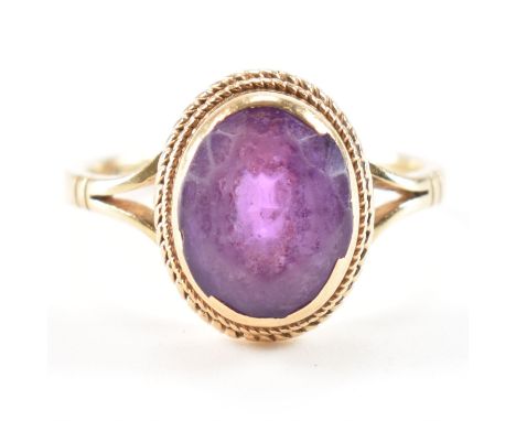 A hallmarked 9ct yellow gold &amp; amethyst ring. The ring having an oval cut bezel set purple stone in a bezel mount to deco