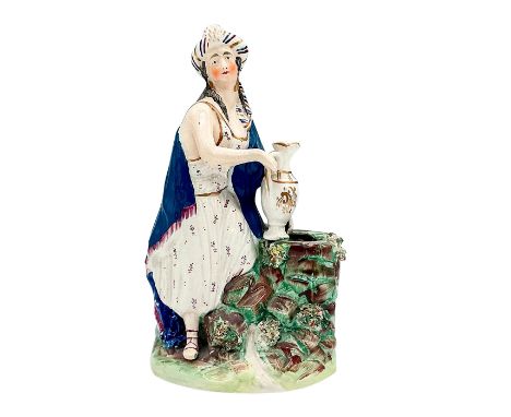 A hand painted earthenware figure depicting the Biblical story from Genesis 24. The wife of Isaac in a blue cloak holding a p