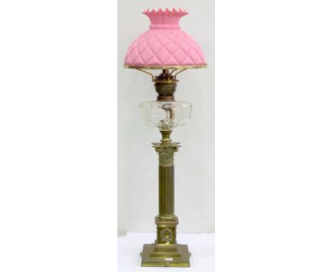 AN EDWARDIAN BRASS CORINTHIAN COLUMN OIL LAMP, WITH FACETED GLASS FOUNT AND BRASS BURNER, PINK QUILTED SATIN GLASS SHADE, 80C