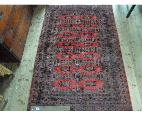 An Eastern-style carpet, having a repeating geometric pattern on a red ground (180cm x 122cm).