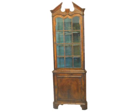 A walnut standing corner cabinet, with a broken pediment, a glazed door above a panel door, on bracket feet, 195cm x 67cm