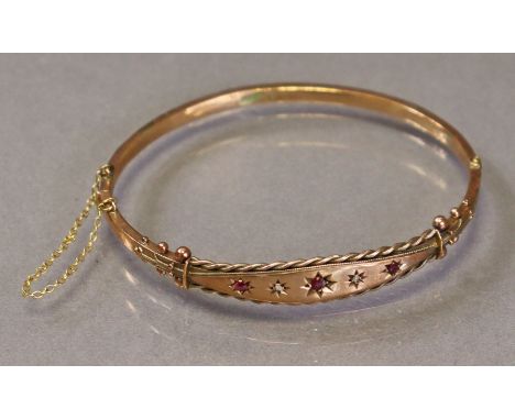 An Edwardian 9ct gold stiff hinged bangle set three small graduated rubies with tiny rose diamonds in between, with safety ch