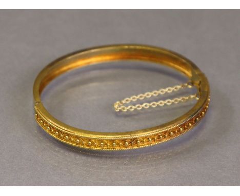 A 15ct gold stiff-hinged bangle with safety chain, one half decorated with applied bead-&amp;-loop design (10.5g).