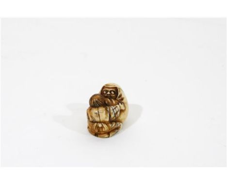 A Japanese carved ivory netsuke of a boy and daruma doll, Meiji period, the young boy kneeling and embracing the egg shaped f