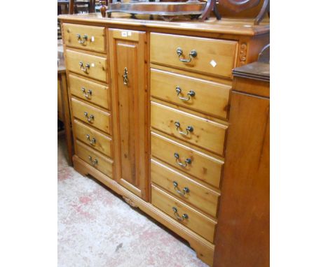 A 1.37m modern polished pine dressing chest with central pull-out fitted drawer and flanking flights of six drawers, set on b