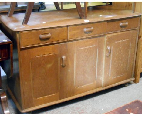 A 1.22m mixed wood Ercol style sideboard with three frieze drawers over bi-folding and single cupboard door, set on Shepherd 