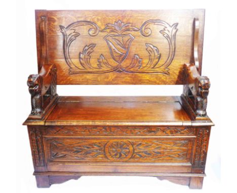 A 1.06m 20th Century polished oak monk's bench with carved decoration, flanking lion pattern supports and locker seat, set on