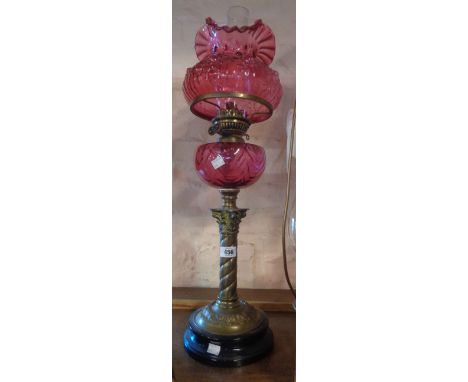 A Victorian table oil lamp with cranberry reservoir on spiral brass column, cranberry shade and chimney