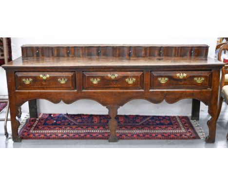 A George III oak dresser, the two-plank top surmounted by a row of serpentine spice drawers, having three raised and fielded 