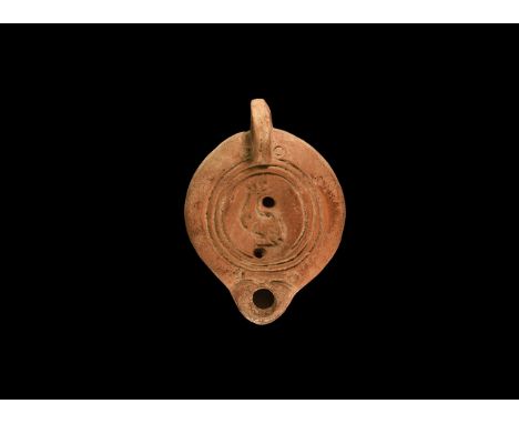 2nd century AD. A ceramic oil lamp, the discus decorated with a stylised dolphin; a pair of ringlets above nozzle and either 