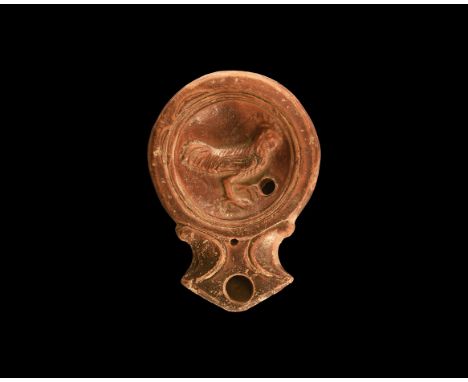 1st century AD. A terracotta oil lamp with circular discus and concentric rims, short nozzle with volute scrolls to the sides