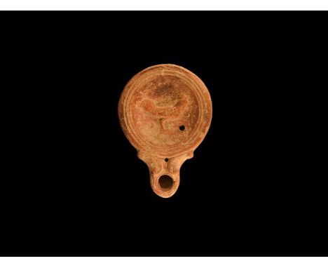 1st century AD. A terracotta oil lamp with flat base, dished discus with concentric rings to the rim, short nozzle with volut