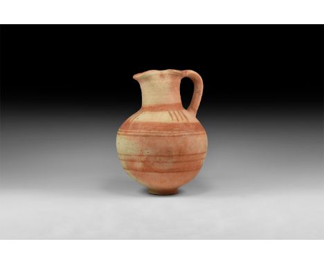 10th-6th century BC. A terracotta globular jug with basal ring, broad tubular neck with pinched sides and pouring lip, strap 