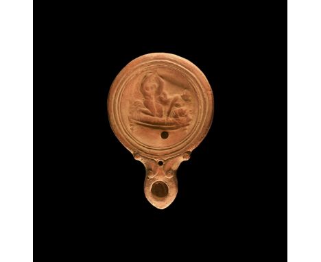 1st century AD. A ceramic oil lamp with rounded nozzle, volutes to the side; dish decorated with erotic scene of man and woma