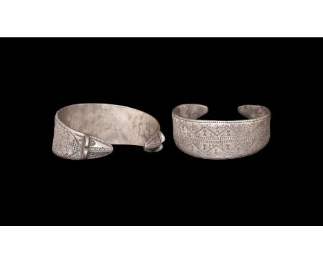 9th-11th century AD. A flat-section silver penannular bracelet with bands of stamped decoration, tapering bear-head finials. 