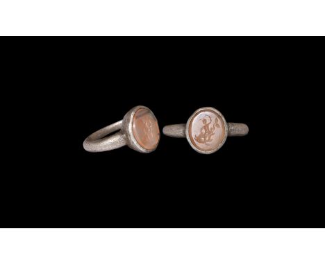 2nd-3rd century AD. A silver finger ring comprising a D-section hoop with angled shoulders, discoid bezel with inset agate cl
