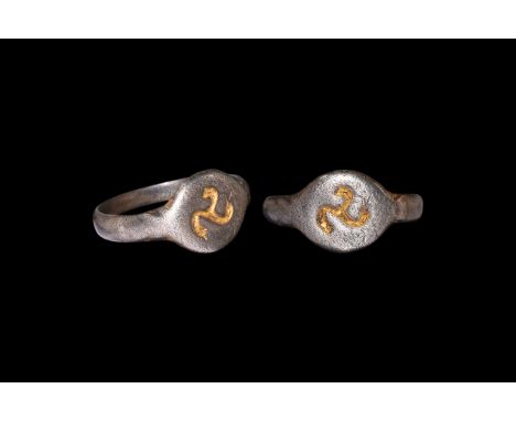 9th-11th century AD. A silver finger ring comprising a D-section hoop, discoid bezel with incuse parcel-gilt triskele motif. 