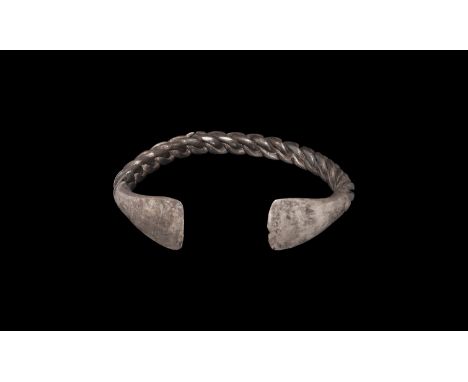 8th-11th century AD. A silver penannular bracelet with triangular-section braided shank and trapezoidal plate finials. Cf. Ne