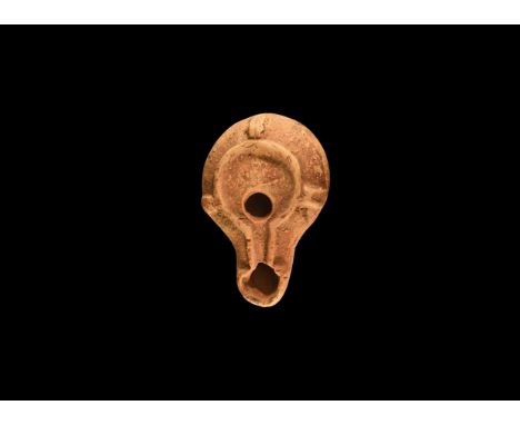 1st-2nd century AD. A terracotta oil lamp with broad nozzle, discus with raised rim, three radiating lugs to the shoulder, ra