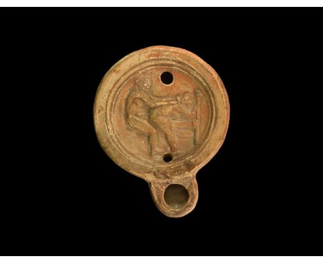 1st-2nd century AD. An unglazed ceramic oil lamp with deep bowl, raised rim to the discus, D-shaped nozzle, erotic scene in l