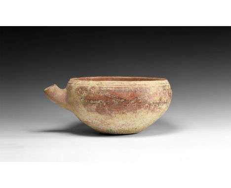 4th millennium BC. A squat ceramic bowl with red glaze, tiered rim, curved spout, raised mask and band of black painted geome