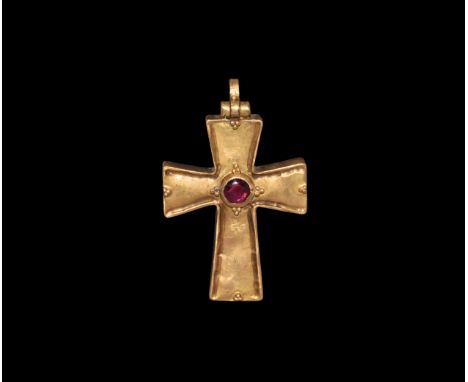 5th-7th century AD. A hollow-formed gold cruciform pendant with hinged suspension loop, central discoid cell with granule det