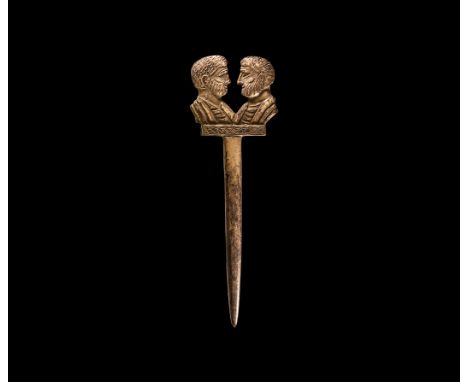 3rd-4th century AD. A bone dress pin with tapering shank, finial formed as two opposed bearded busts on a hatched base. 6.11 