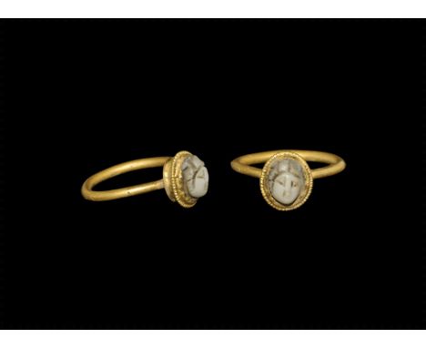 ROMAN GOLD RING WITH CAMEO BUST. 1st century AD. A round-section gold hoop with drum bezel and beaded wire fillet, inset chal