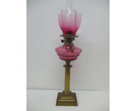 A Victorian brass oil lamp with a clear glass chimney, a contemporary matched shade, and a cranberry glass reservoir, on a re