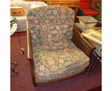 An Ercol bergere armchair with green floral cushions within caned ends