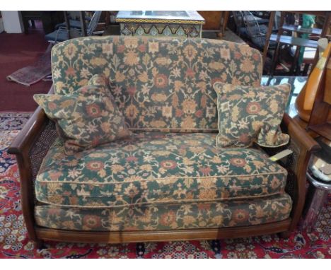 An Ercol two seater bergere sofa with green floral cushions within caned ends