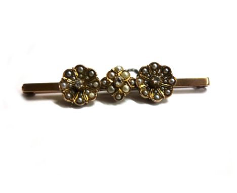 An early 20th century gold, half pearl and diamond bar brooch, in the form of three stylised flowerheads, each with a small c