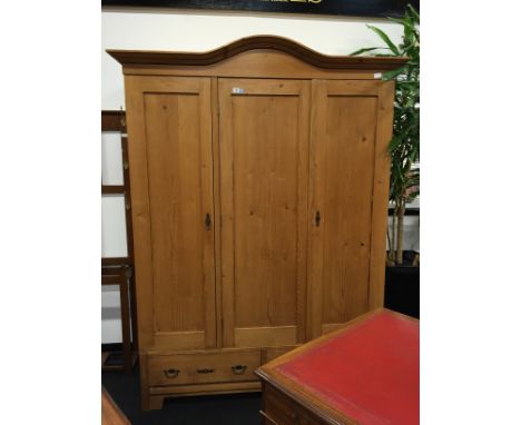 A large arched top three drawer stripped pine wardrobe with two drawers below, panel backed interior, resting on bracket styl