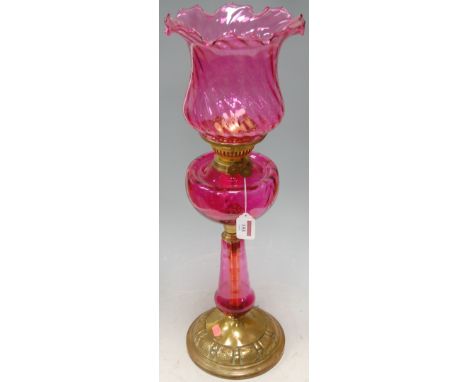 A Victorian cranberry glass pedestal oil lamp, having a later glass shade above glass reservoir on a brass circular base Cond