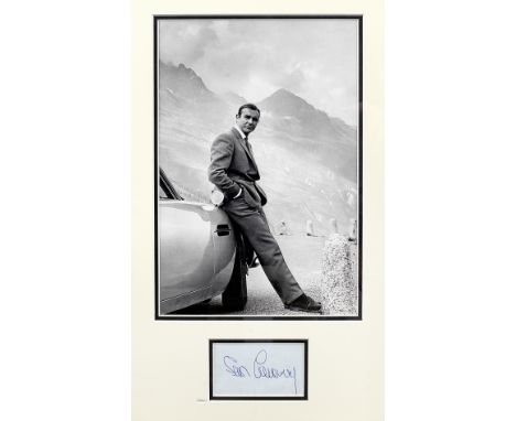 A photograph of Sean Connery as 007 with the Goldfinger Aston Martin DB5 in the Furka Pass, mounted with an autograph,monochr