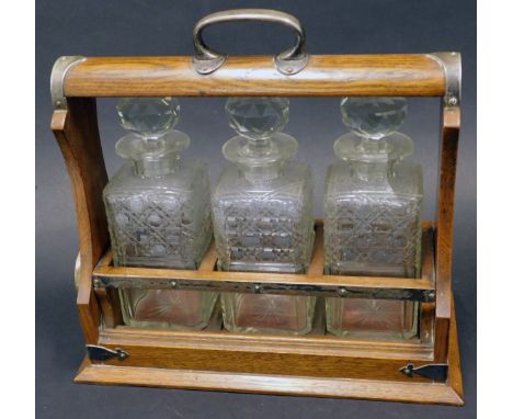 An Edwardian oak and silver plated tantalus, with four cut glass square section decanters and faceted stoppers, with a key, 3