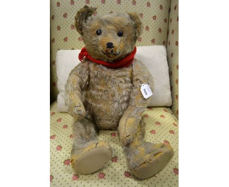 An early 20th century silver plush teddy bear, probably Steiff, with composite eyes, stitched nose and mouth, swivelling head