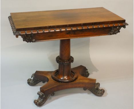 A William IV rosewood veneered card table the rectangular figured top above a frieze reel and foliate carved, the cylindrical