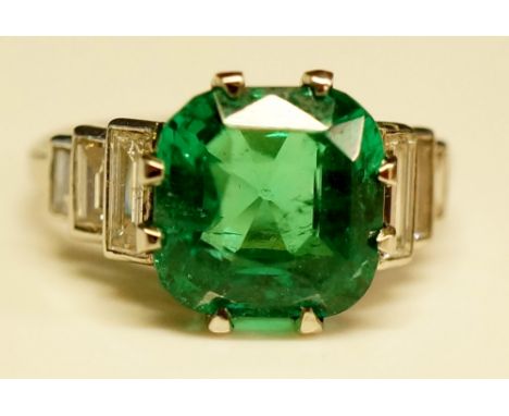 An emerald and diamond ring, the Columbian natural cushion shaped emerald flanked by step cut diamond shoulders, the emerald 