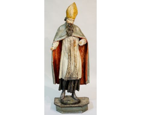 A 17th Century Continental polychrome decorated carved wooden figure of a bishop, standing, with red lined grey cloak and whi